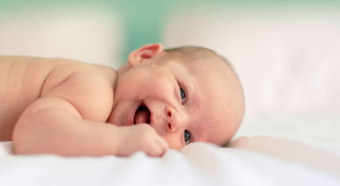 Bebê sorrindo deitado em uma cama com fundo suave