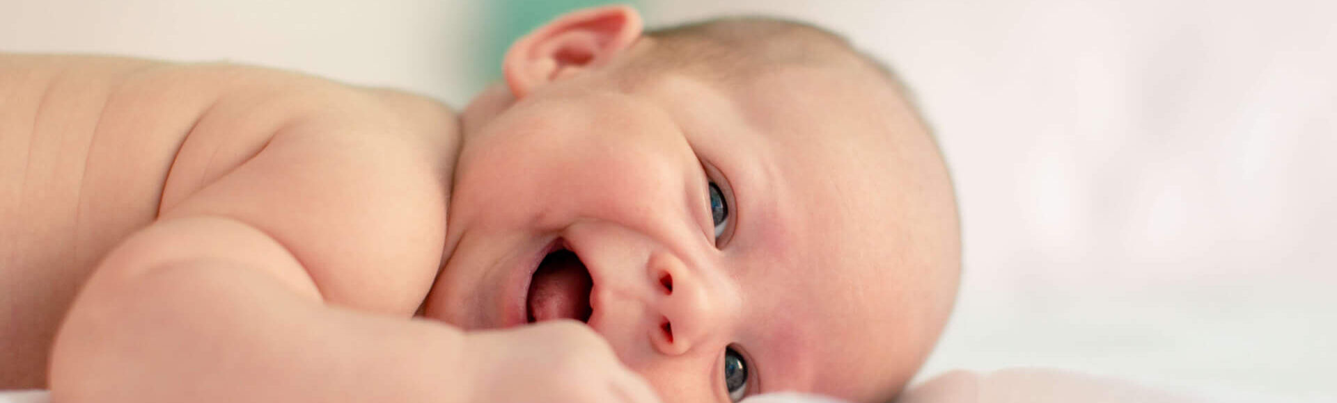 Bebê sorrindo deitado em uma cama com fundo suave