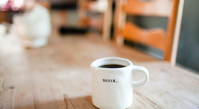 Xícara de café com a palavra "BEGIN" sobre uma mesa de madeira.
