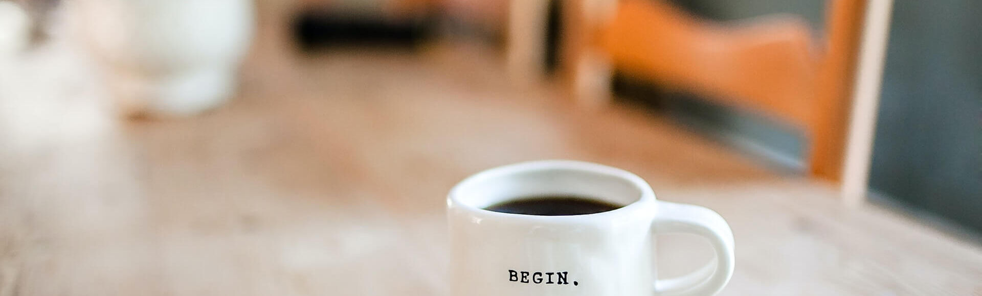 Xícara de café com a palavra "BEGIN" sobre uma mesa de madeira.