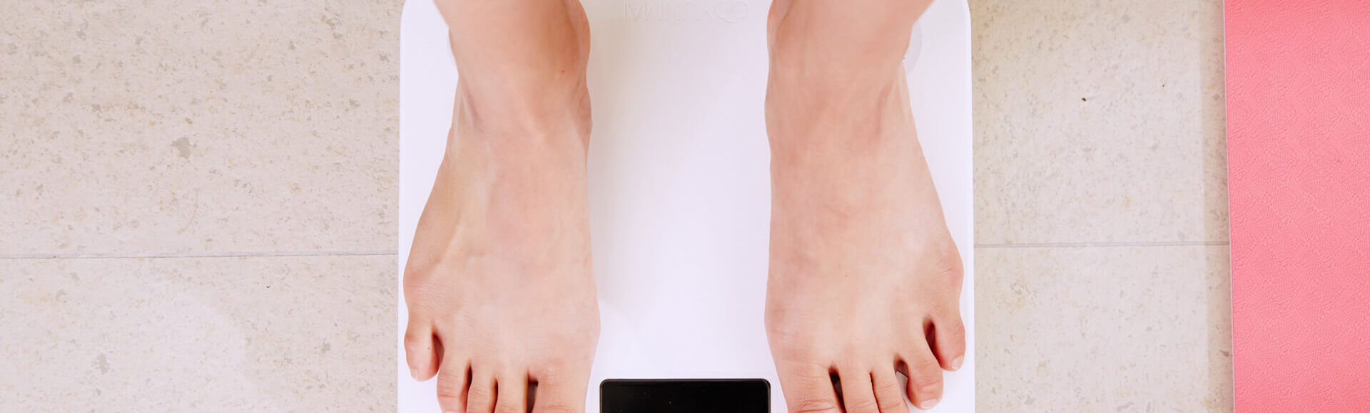 Pessoa se pesando em balança. A foto mostra os pés sobre balança de uso doméstico.