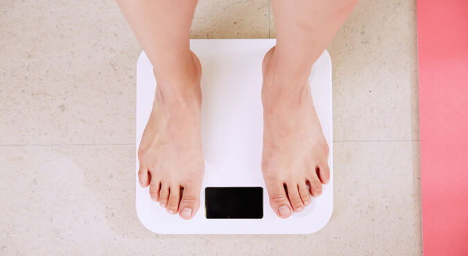 Pessoa se pesando em balança. A foto mostra os pés sobre balança de uso doméstico.