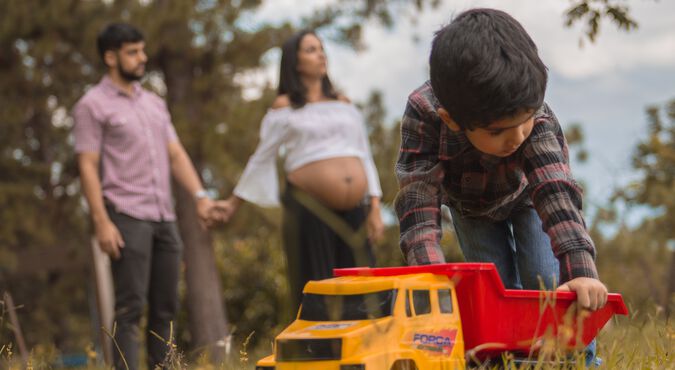 Família composta por pai, mãe gestante e filho mais velho em parque