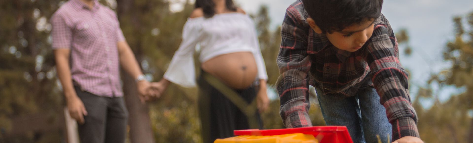 Família composta por pai, mãe gestante e filho mais velho em parque