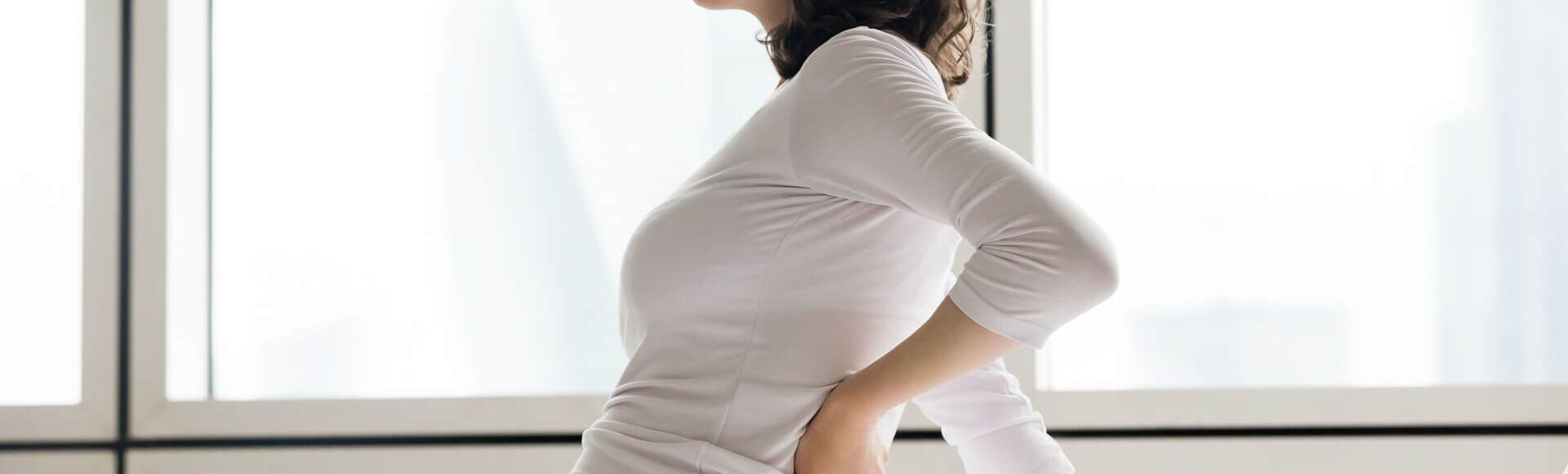 Gestante sentada com a mão nas costas em expressão de desconforto