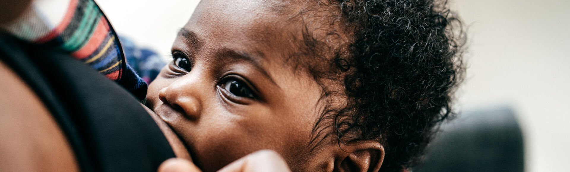 Bebê de cabelo cacheado sendo amamentado no colo da mãe