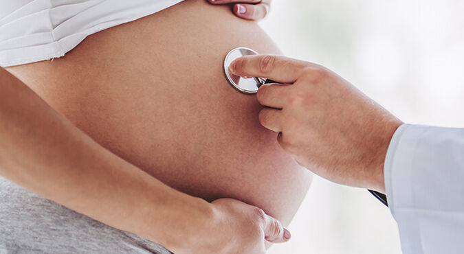 Profissional de saúde posicionando estetoscópio sobre barriga de gestante