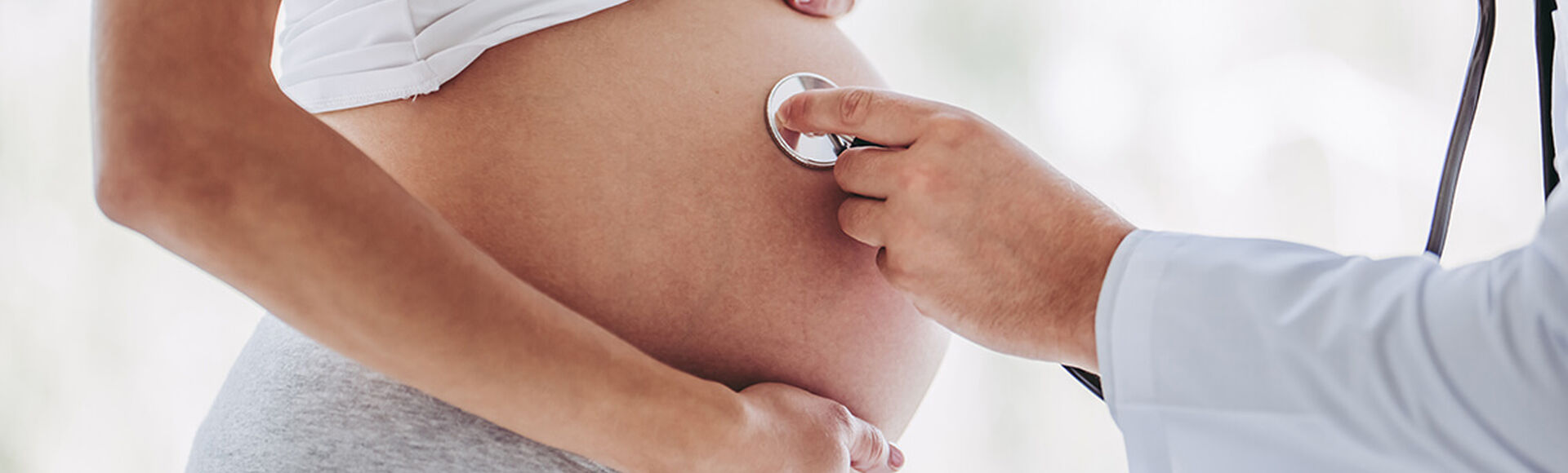 Profissional de saúde posicionando estetoscópio sobre barriga de gestante