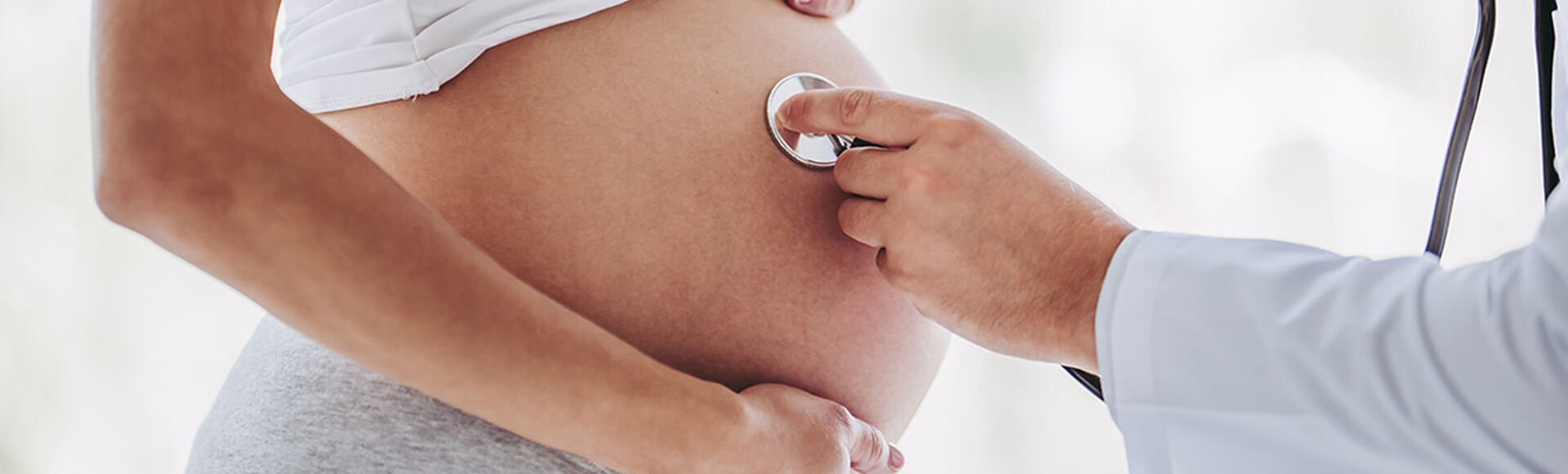 Cuidado médico durante a gestação | Seus Abraços Inspiram os Nossos - Huggies® Brasil Profissional de saúde posicionando estetoscópio sobre barriga de gestante