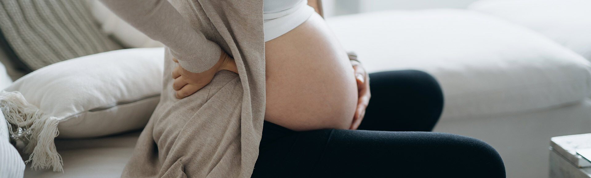 Gestante branca sentada com pernas cruzadas em frente ao corpo e mãos apoiadas na coluna lombar