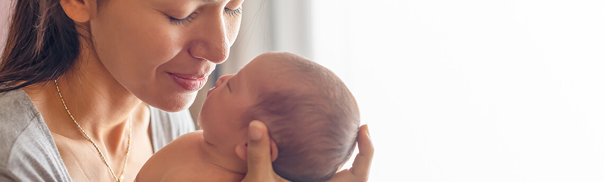 Mãe segurando bebê recém-nascido próximo a seu rosto em momento de carinho