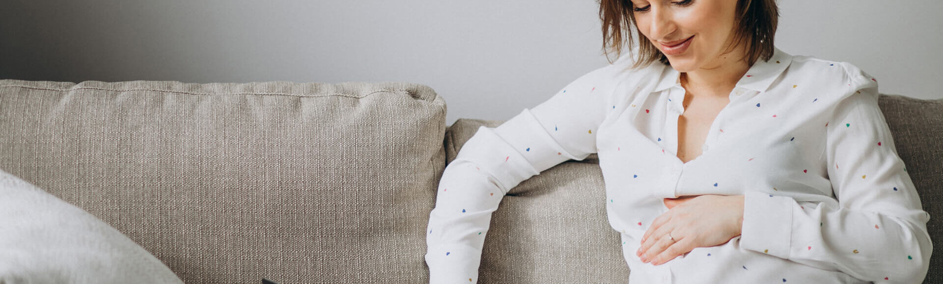 Trabalho durante a gravidez - Seus Abraços Inspiram os Nossos - Huggies® Brasil Gestante sentada com a mão na barriga enquanto usa um computador notebook
