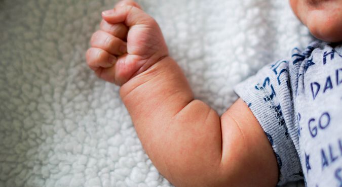 Bebê deitado na cama com os braços abertos