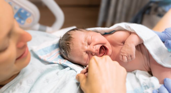 Mulher branca logo após parto com bebê recém-nascido nos braços