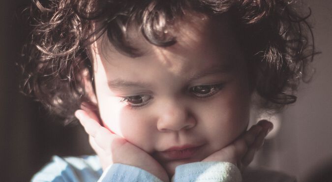 Criança com as maõs no rosto demonstra excesso de timidez na infância