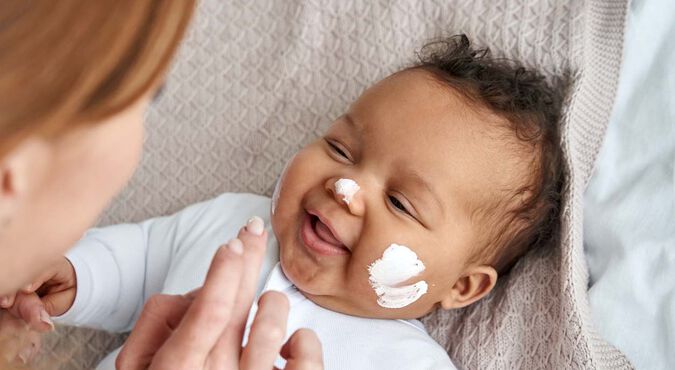 Bebê sorrindo enquanto recebe cuidados na pele.