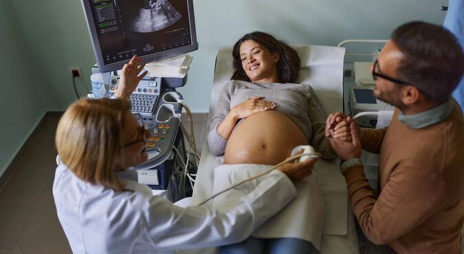 Mulher grávida sorrindo durante exame de ultrassom, segurando a mão do parceiro