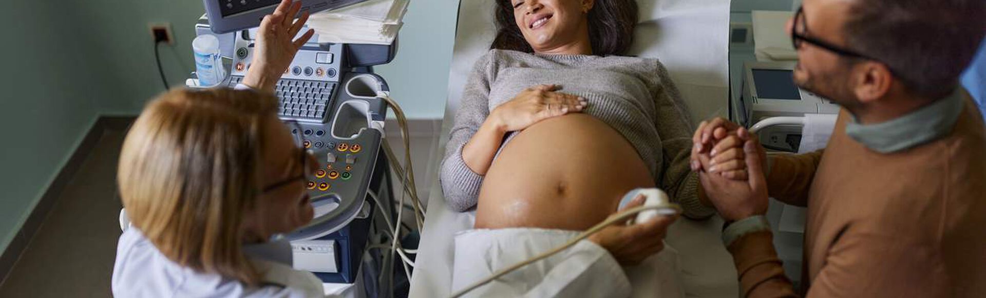 Mulher grávida sorrindo durante exame de ultrassom, segurando a mão do parceiro