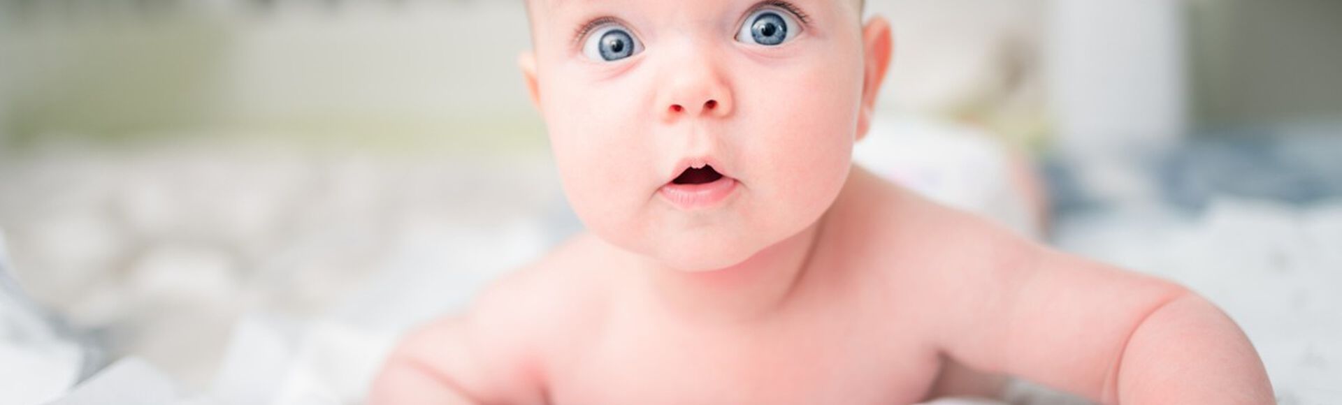 Bebê branco deitado de bruços com olhos azuis bem abertos