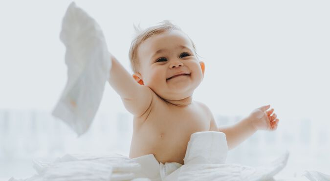 Bebê  sorridente sentado junto a pilha de fraldas