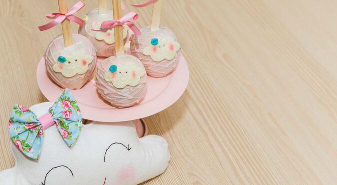 Centro de mesa com maçãs do amor confitadas com chocolate rosa, com tema de nuvenzinha. Ao lado, uma nuvem de pelúcia com lacinho.