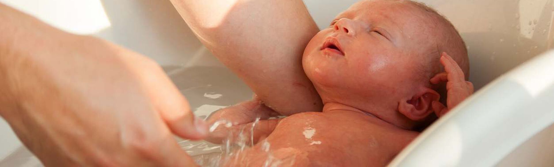 Bebê recém-nascido brincando com cuidadora que segura sua cabecinha com segurança, enquanto dá o seu banho.