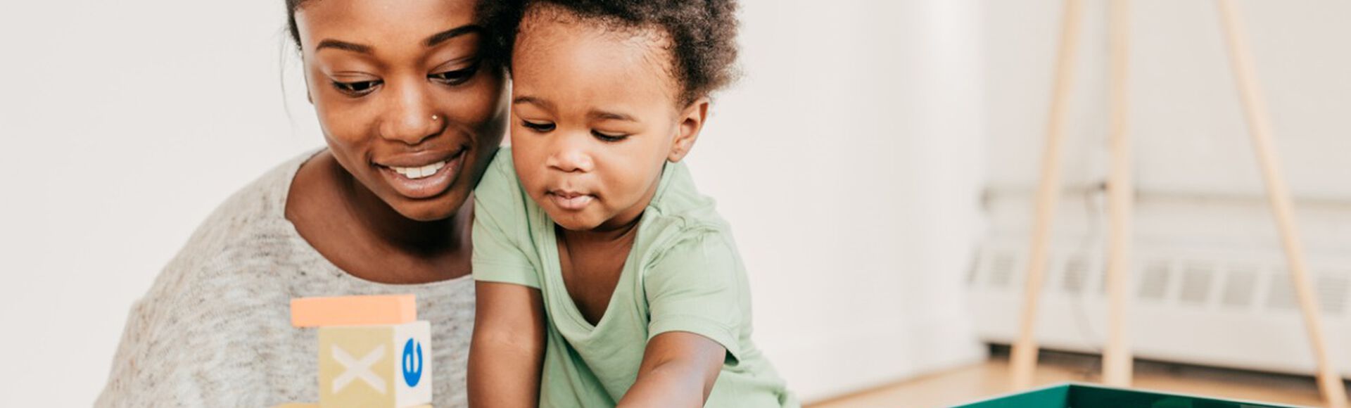 Mãe e bebê brincam felizes com blocos de montar, em artigo sobre visão do bebê. Ambos são negros e vestem roupas claras