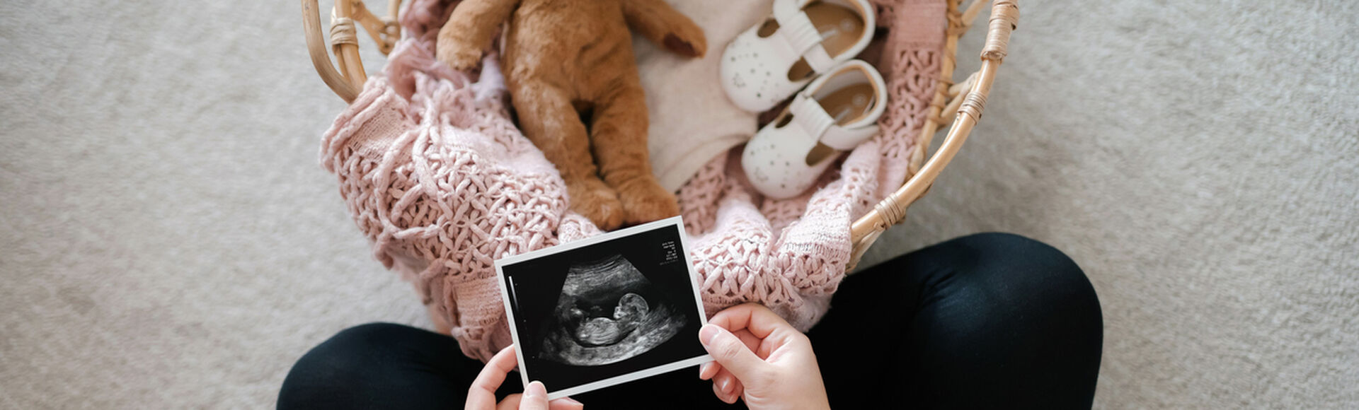 Gestante segurando ultrassom em frente a cestinho de bebe