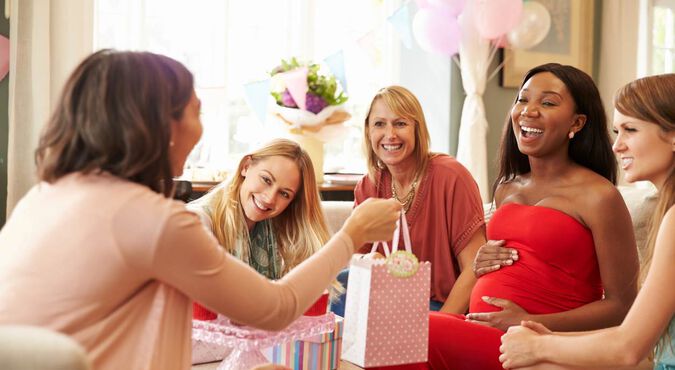 Mulheres sorrindo durante um chá de bebê com presentes.