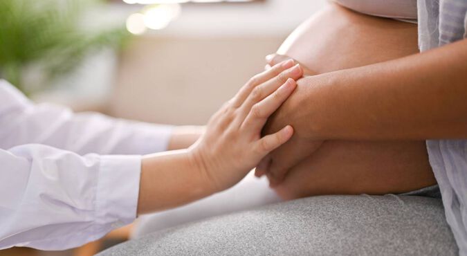 mulher grávida com as mãos de outra pessoa tocando sua barriga