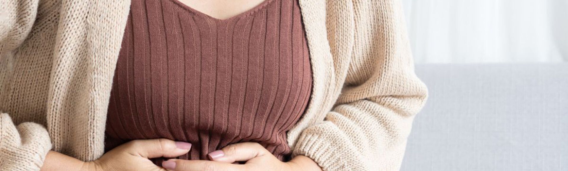 Mulher sentada com as mãos no abdômen em sinal de desconforto