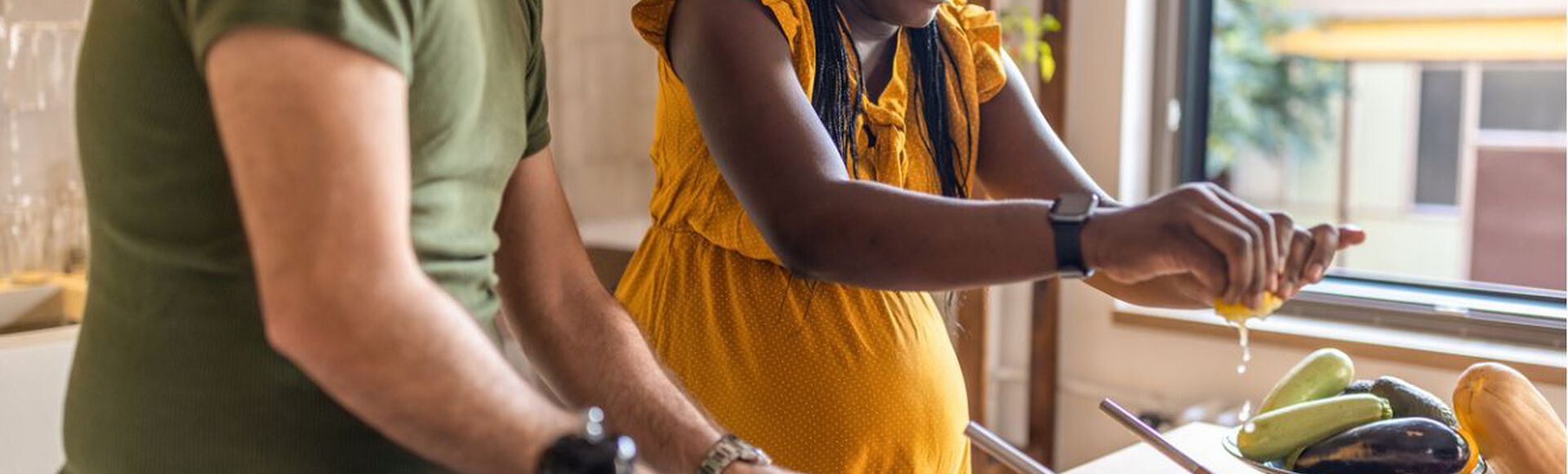 Mulher negra grávida e homem branco cozinhando juntos