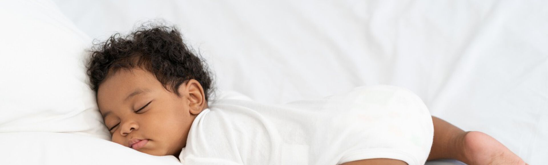 Bebê recém-nascido deitado ao lado da mãe em cama com lençóis brancos