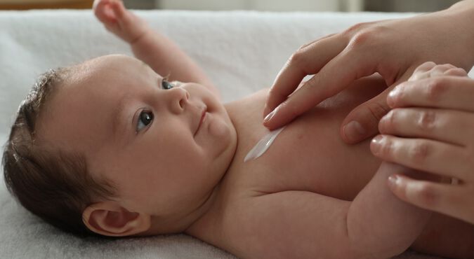 Bebê deitado sendo cuidado e recebendo pomada