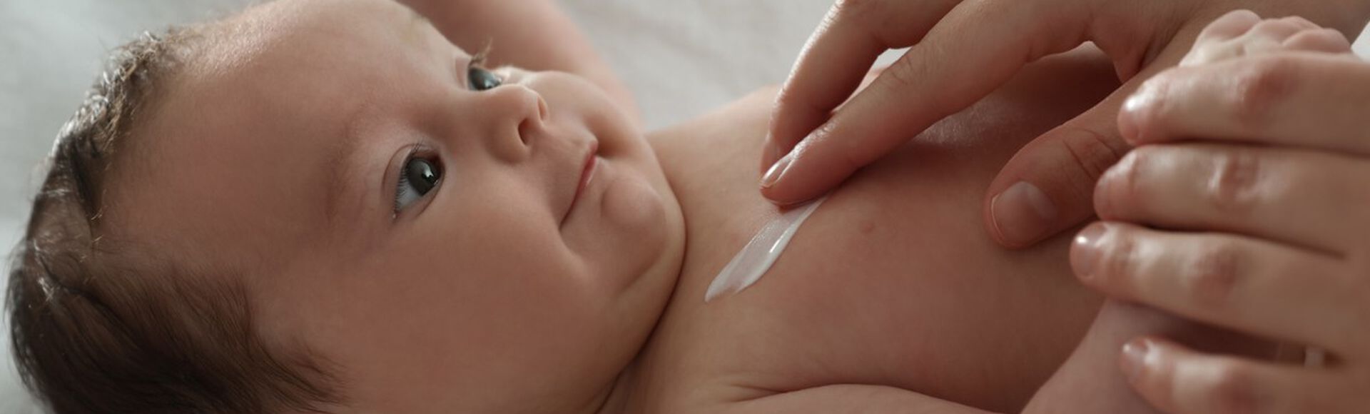 Bebê deitado sendo cuidado e recebendo pomada