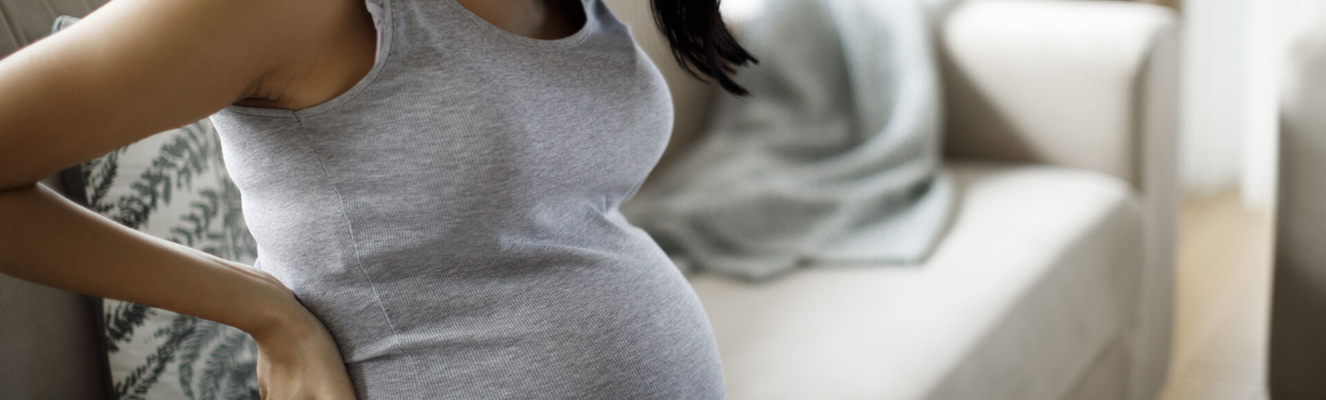 Gestante sentada em sofá com mãos na lombar