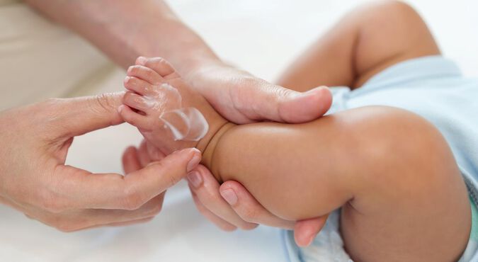 Detalhe de mãos massageando pezinho de nenê com hidratante à base de manteiga de cacau.