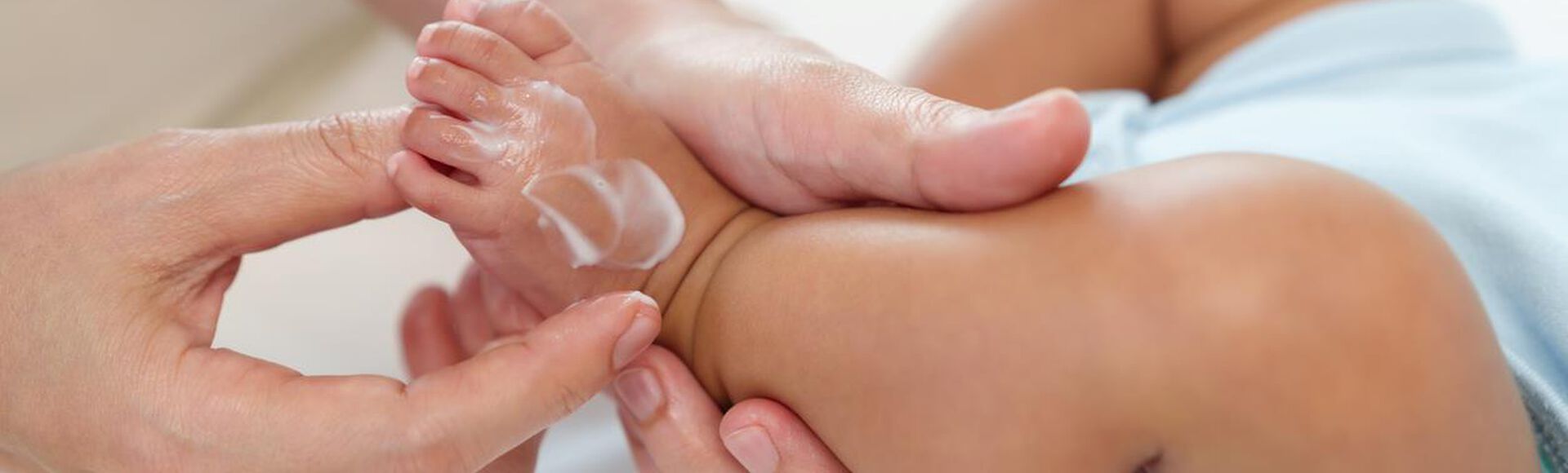 Detalhe de mãos massageando pezinho de nenê com hidratante à base de manteiga de cacau.
