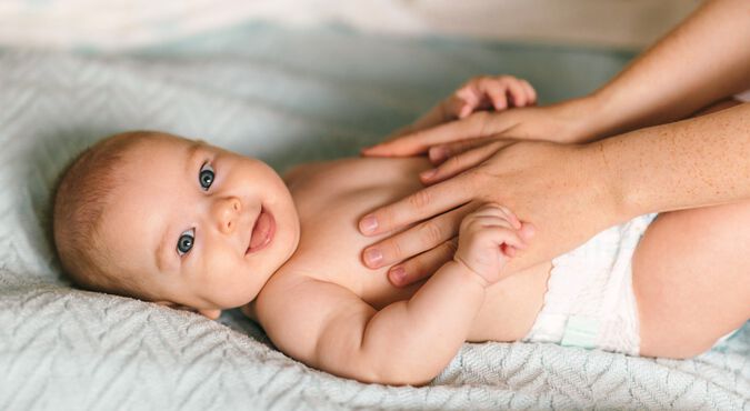 Bebê branco deitado em cama sorridente recebendo massagem