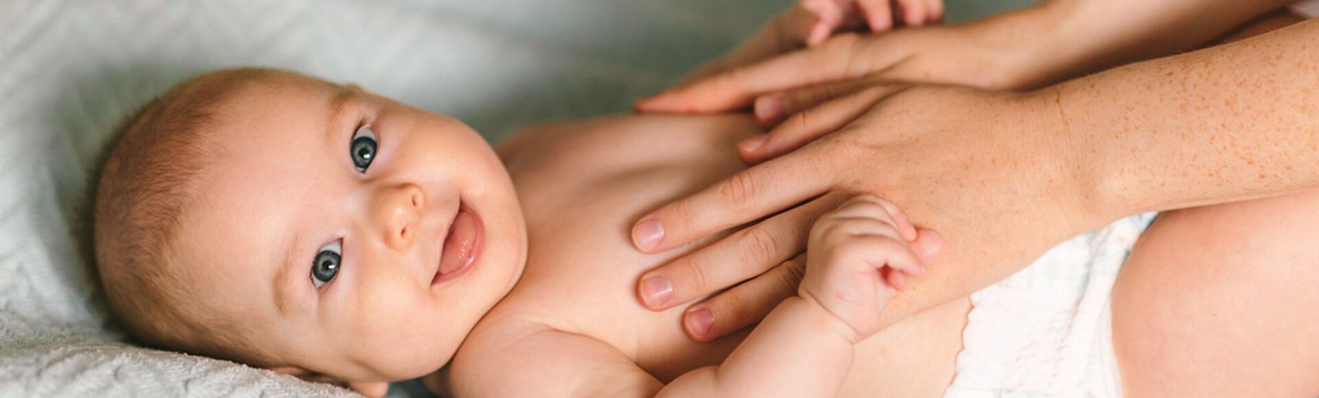 Bebê branco deitado em cama sorridente recebendo massagem