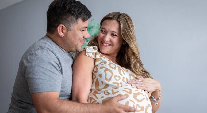 Casal sorrindo enquanto o marido segura a barriga da esposa grávida.