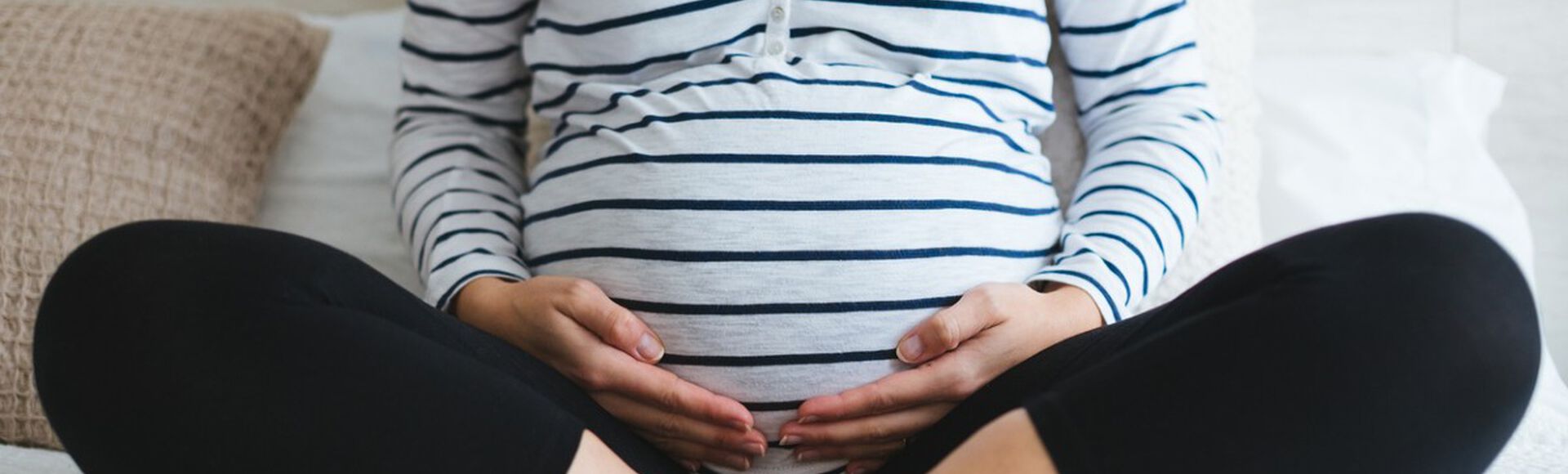 Gestante sentada com pernas cruzadas e mãos na barriga