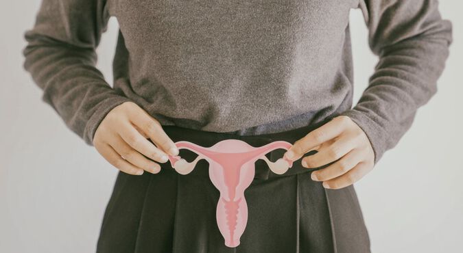 Mulher vestindo calças e blusa cinza segurando uma imagem de útero em frente ao ventre