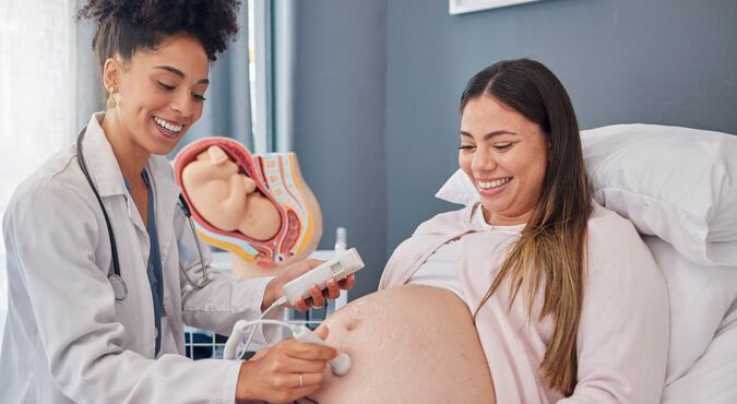 Grávida fazendo ultrassom. Ela e a ginecologista parecem muito confortáveis uma com a outra, e sorriem com ternura.