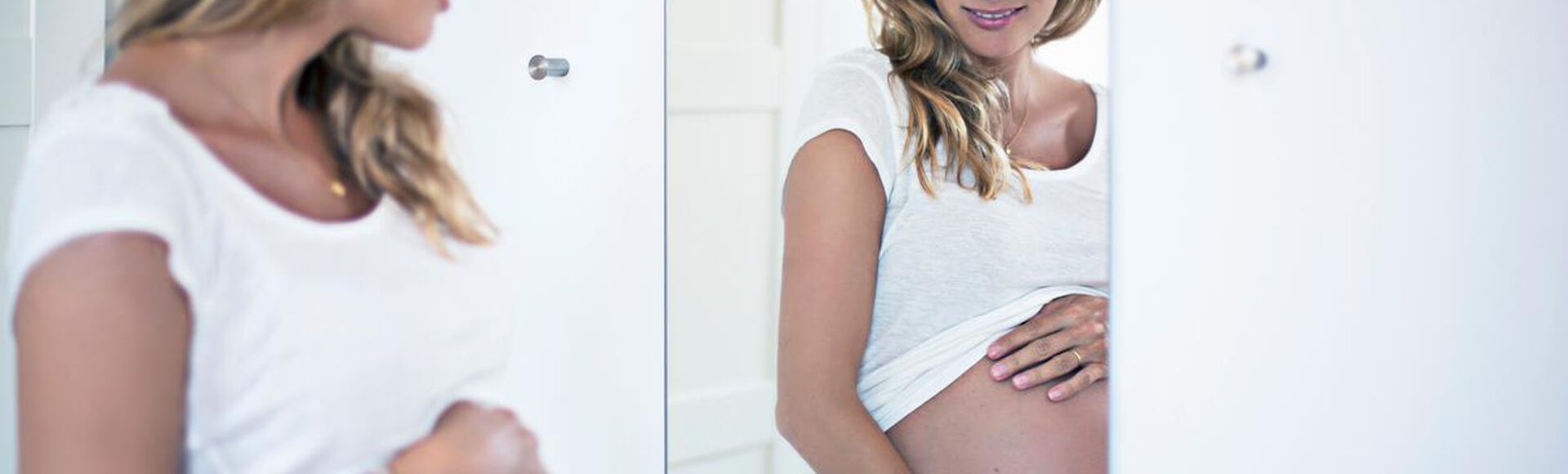 Mulher grávida admirando sua beleza em frente a um espelho, enquanto acaricia sua barriga gentilmente.