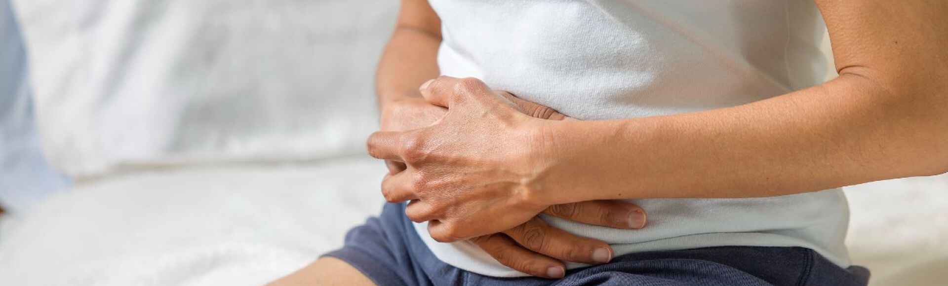 Mulher sentada na beira da cama com as mãos envolvendo a barriga