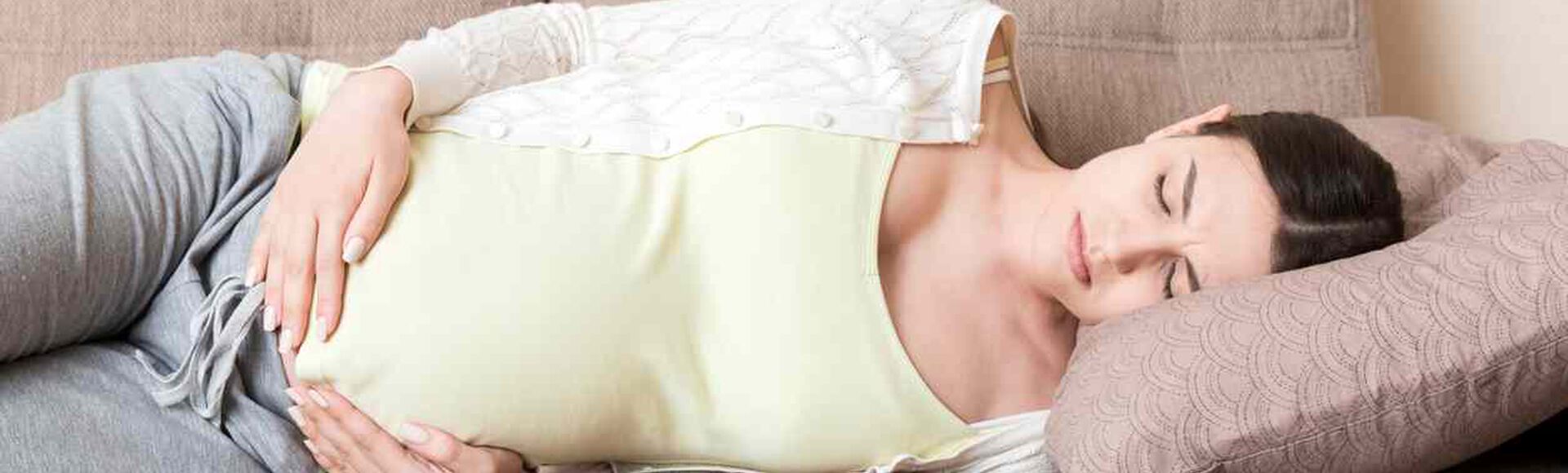 Mulher grávida ao celular, com uma mão no pé da barriga e fisionomia de dor