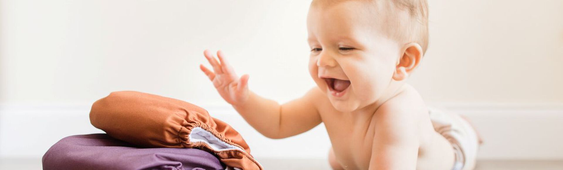 Bebê de bruços, sorrindo, dando tapinha em pilha de fraldas reutilizáveis.