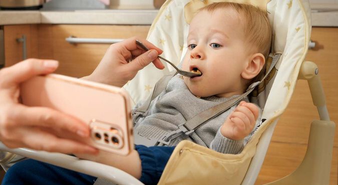 Bebê sendo alimentado enquanto assiste a algo em um celular.