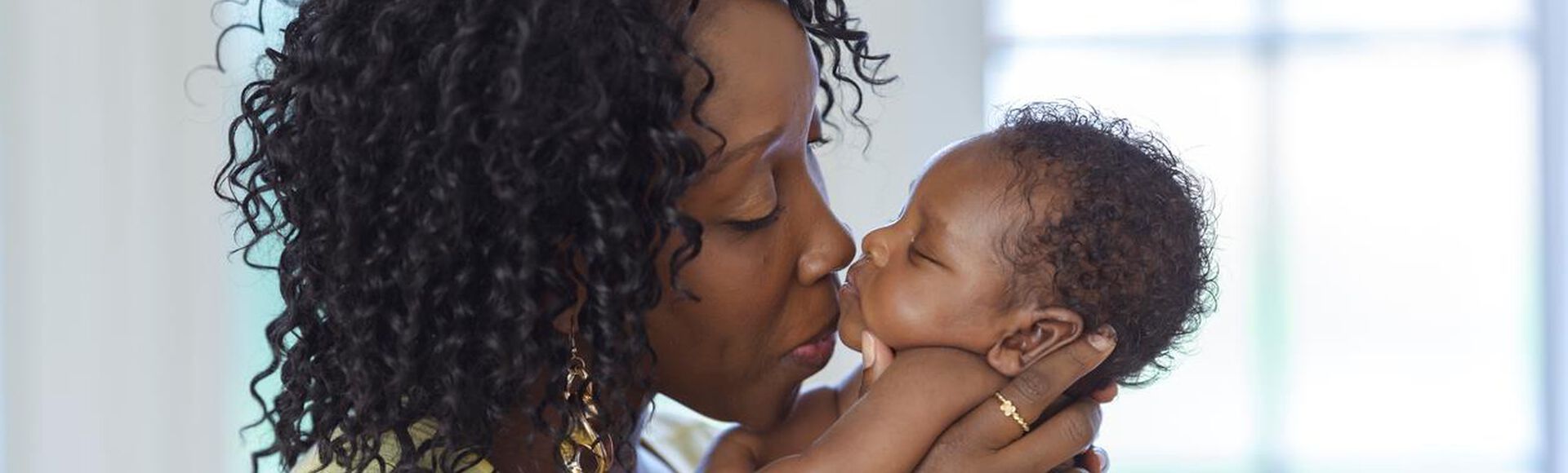 Mãe beijando seu bebê com cabelo cacheado